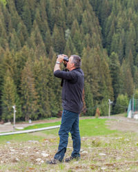 Side view of mature man looking through binoculars in forest