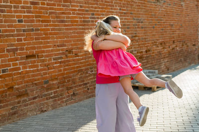 Side view of young woman standing against brick wall