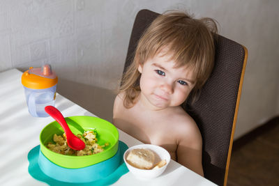A joyful toddler girl sits in her high chair at home, eating scrambled eggs and toast for breakfast. 