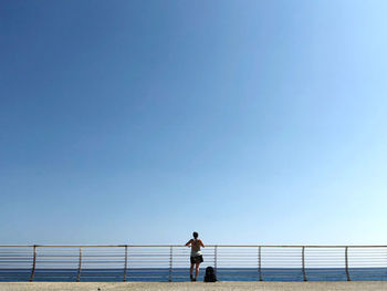Man standing on railing against clear blue sky