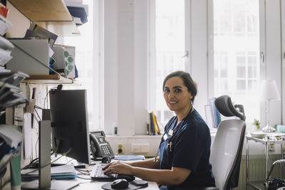 Side view portrait of female nurse sitting at desk with computer in clinic