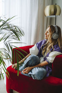 Smiling woman wearing headphones enjoying on armchair in studio