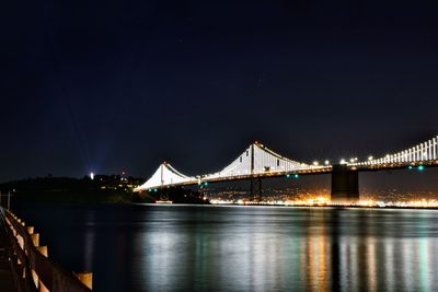 Illuminated bridge over calm river at night