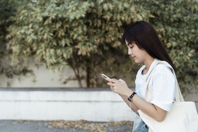 Side view of young woman using mobile phone outdoors