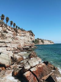 Rock formations by sea against clear blue sky