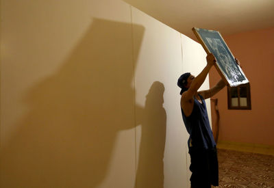 Man holding umbrella standing against wall at home