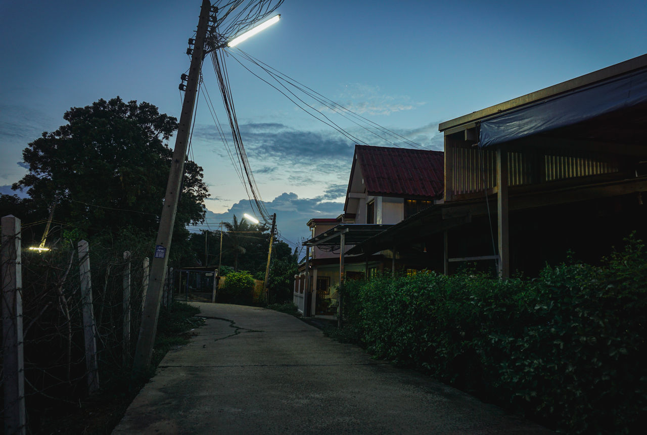 ROAD AMIDST PLANTS AND BUILDINGS AGAINST SKY