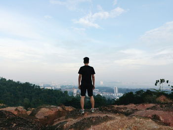 Rear view of man standing on rock against sky