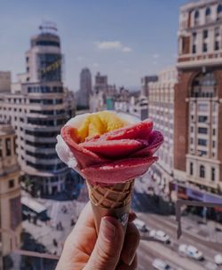 Hand holding ice cream cone against buildings in city
