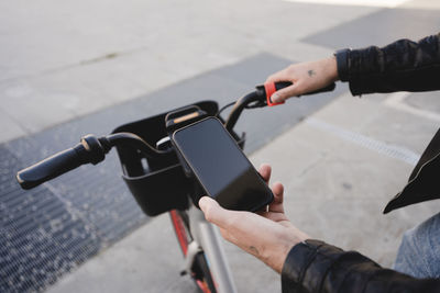 Hand of man renting bicycle through mobile phone on footpath