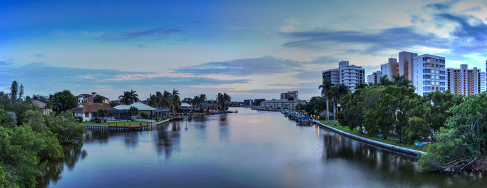 Panoramic view of buildings by river against sky in city