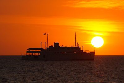 Silhouette ship in sea against orange sky