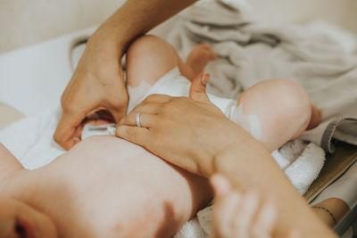 Cropped hands of mother changing daughter diaper on bed at home
