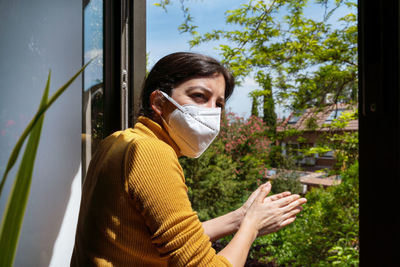 Woman wearing mask clapping while standing by railing against plants during quarantine