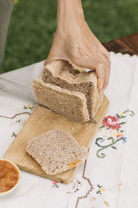 Female hand cutting bread on cutting board in garden