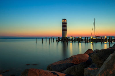 Lighthouse by lake against sky during sunset