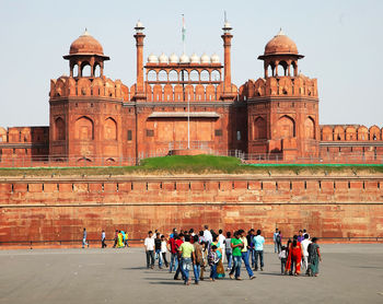 People walking by the red fort against clear sky