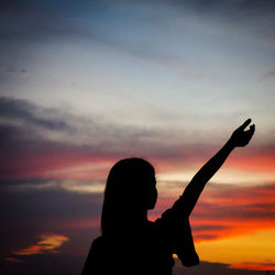 Silhouette woman with arms raised against sky during sunset