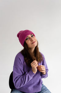 Beautiful young woman in purple hat and sweatshirt on gray background in studio