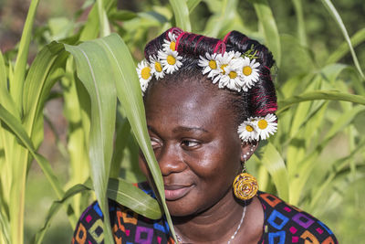 African woman with hair rollers and daisy flowers in her hair with cornfield in the background.
