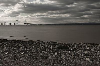 View of suspension bridge over river against cloudy sky
