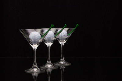 Golf balls and tees in martini glasses on black background