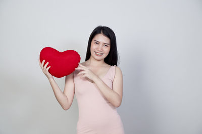 Portrait of smiling woman holding heart shape over white background