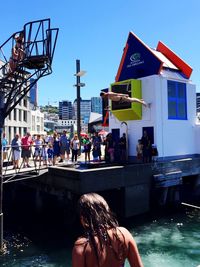 Man diving into lake with people watching against clear blue sky in city