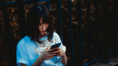 High angle view of woman using mobile phone while sitting against fence