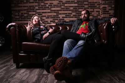 Full length of couple resting on sofa against brick wall