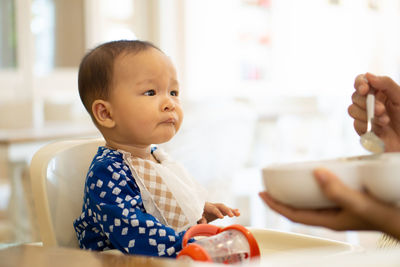 Cropped hands of mother feeding food to daughter sitting on high chair at home