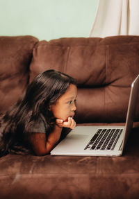 Cute girl using laptop while lying on sofa at home