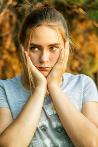 Teenage girl looking away while touching her cheeks outdoors