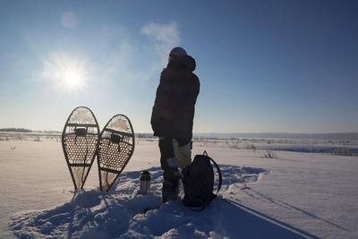 Rear view of man standing on snow covered field against sky on sunny day