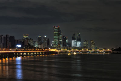 Illuminated city by river against sky at night