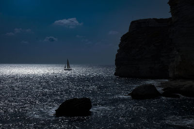 Silhouette rock formations by sea against sky