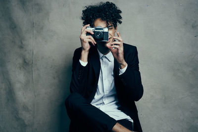 Young man photographing while sitting on wall