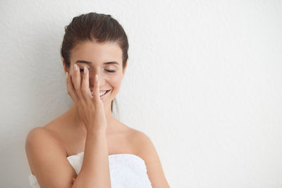 Smiling young woman wearing bathrobe standing against wall