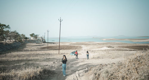 People walking on road by sea against clear sky