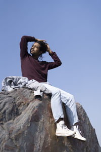 Low angle view of woman sitting on rock against clear sky