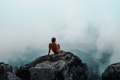 Rear view of man sitting on rock against mountain