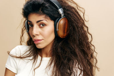 Portrait of woman wearing wireless headphones standing against wall