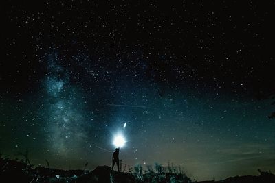 Silhouette man holding illuminated flashlight against star field