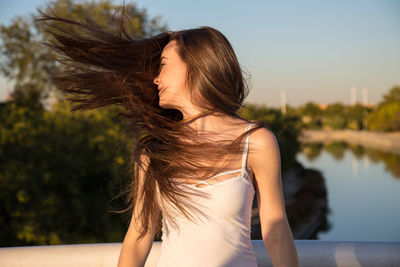 Young woman with tousled hair standing by railing over river