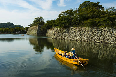 People in boat by trees on lake against sky