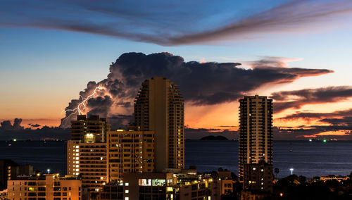 Illuminated buildings in city against sky during sunset