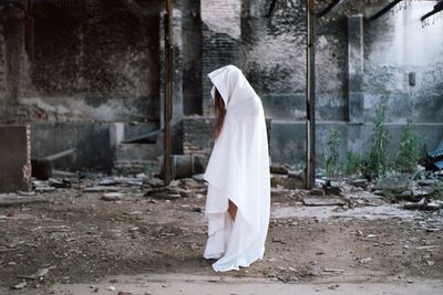 Woman covered with white textile standing in abandoned building