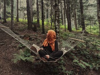 Full length of woman sitting on hammock in forest