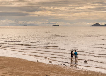 High angle view of couple standing at beach against cloudy sky