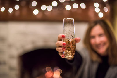 Smiling mature woman holding champagne flute against defocused lights